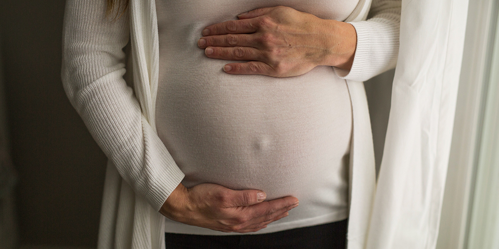 Ciężarna kobieta stojąca przy oknie trzyma swój brzuch Ciężarna kobieta stojąca przy oknie trzyma swój brzuch